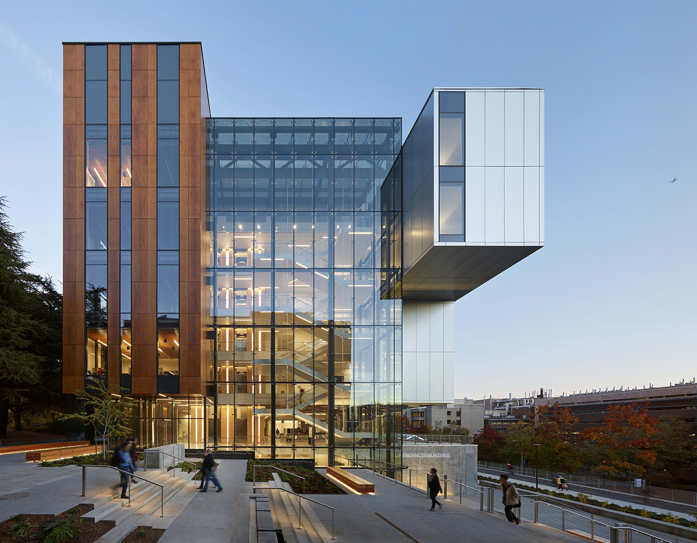 View of the west facade of the Life Sciences Building at dusk with students walking by on the outdoor steps.