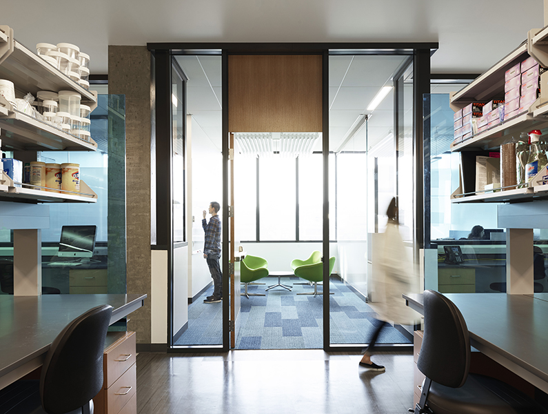 View from research lab looking out to a collaboration space with a man drawing on a white board