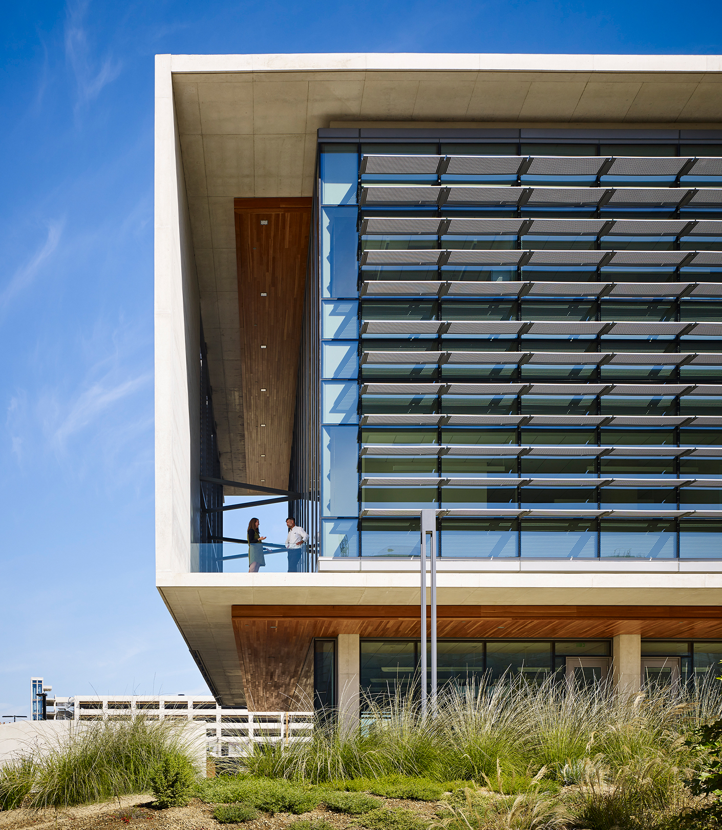 Exterior view of south west corner with two people standing and talking on outdoor balcony.