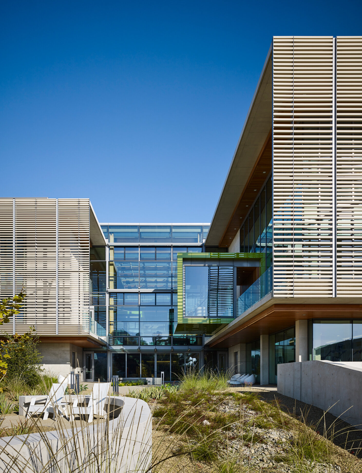 West exterior with white adirondackchairs outside and green pod jutting out from atrium