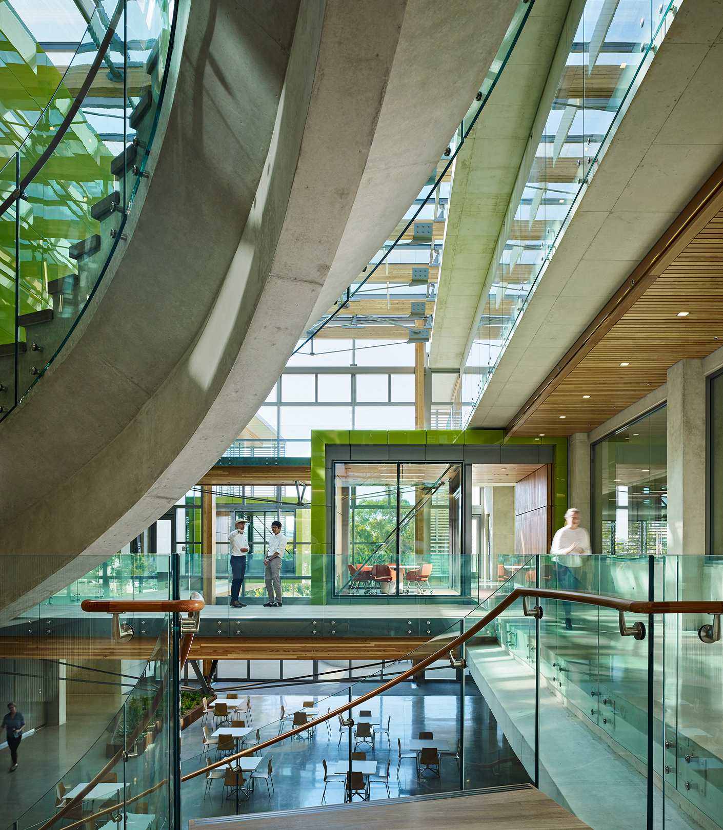 Bright interior atrium with meeting pods jutting out and pedestrian bridges where two men have stopped to talk