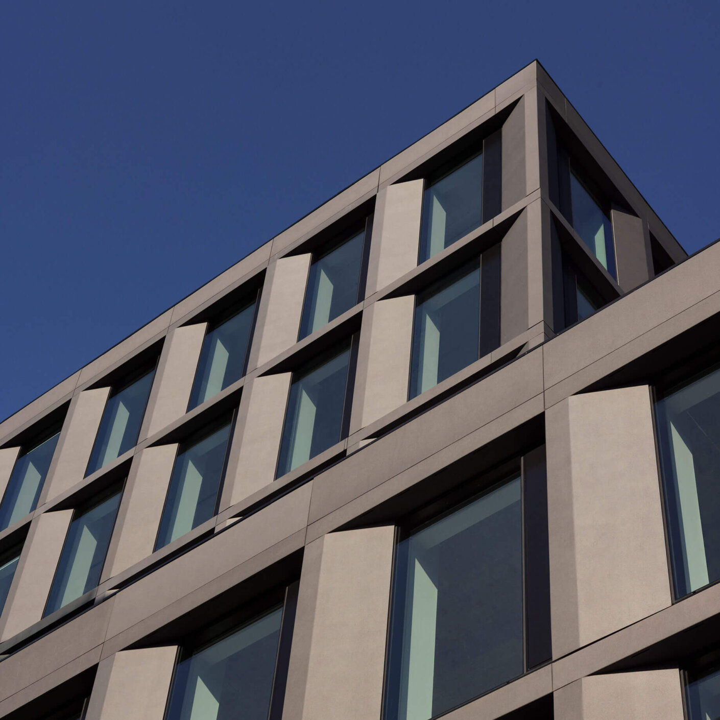 A view of the top corner of the building from below with sunlight defining the geometric form of the innovative glass-fiber reinforced concrete exterior cladding panels.
